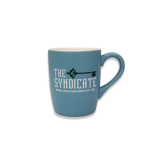 A blue ceramic coffee mug with 'the syndicate' text and a graphic of a key.
